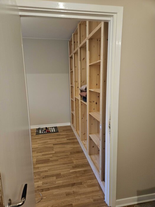 Träbyggd garderob utan dörrar, placerad i ett rum med trägolv. Hyllorna byggda av 18mm skivor och 21mm plankor.