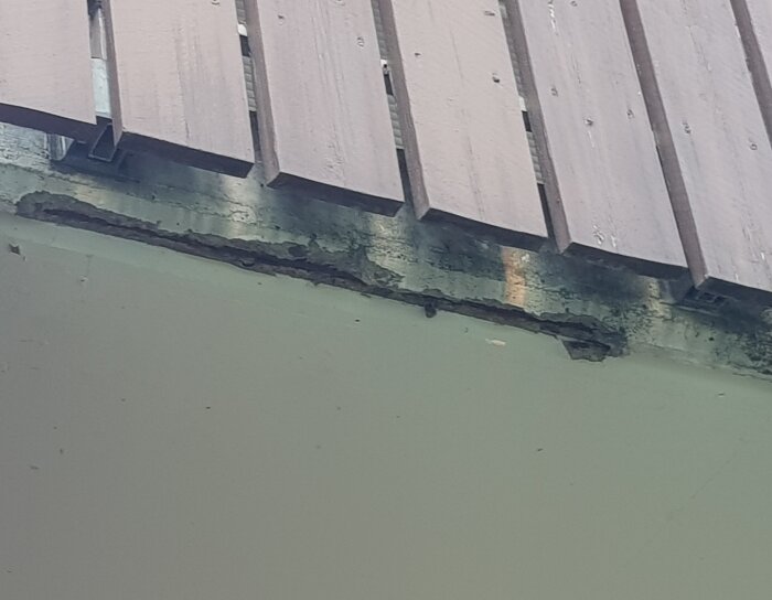Sprucken betong på undersidan av balkong från 60-talet, med spricka vid infästning av balkongräcke.