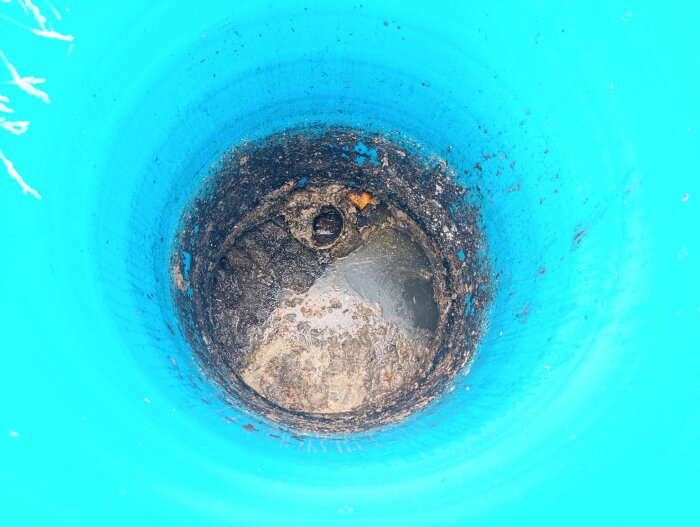 Invändig vy av en septiktank, visar smutsigt vatten och avlagringar längs väggarna i en blå behållare. Ingen tydlig tömning synlig.