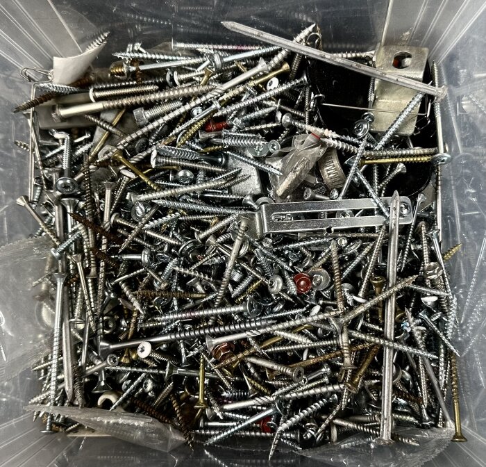 En plastlåda fylld med blandade skruvar, bultar och små metallföremål för sorteringsprojektet "Slasken".