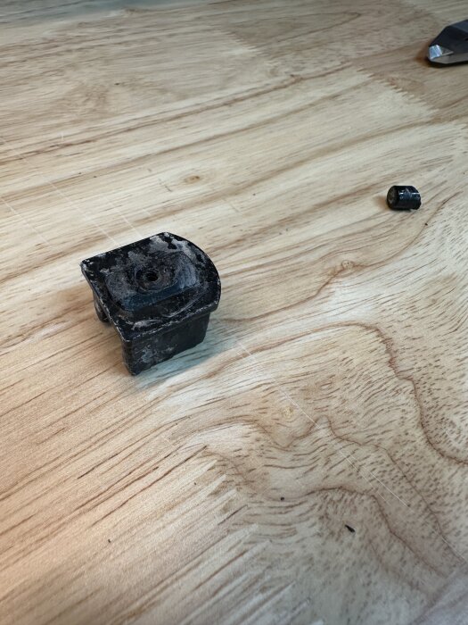 Svart plastdel och lös rund plastbit på träbord, del av duschdörrmekanism.