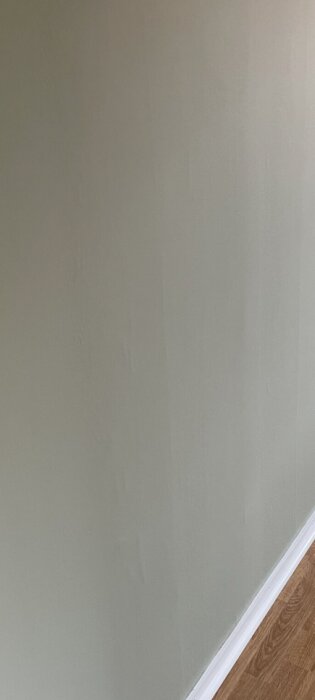 En slät vägg med subtila ojämnheter och en vit golvlist, vilket indikerar mindre kvalitet i utförande.