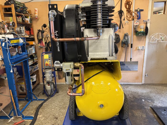 Kompressor med installerad oljekylare och kopplingar i ett verkstadsutrymme.