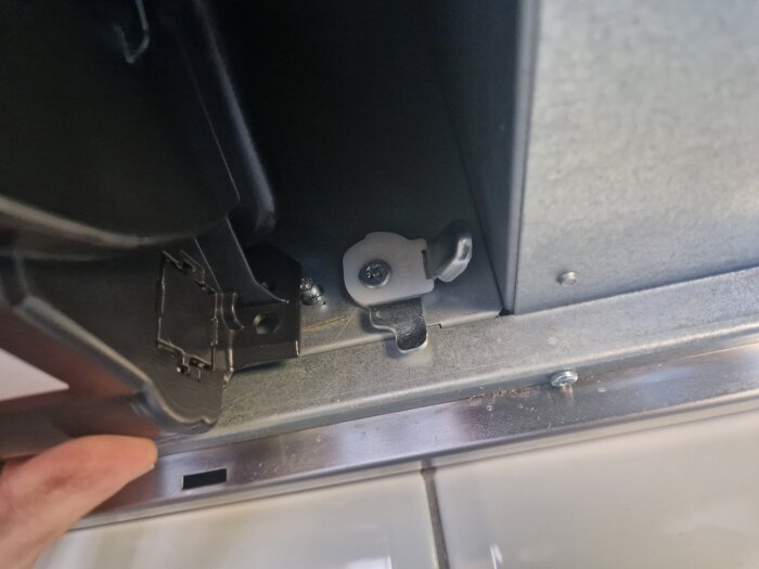 Köksfläktsinstallation med synliga låsbleck och skruvar innanför metallhöljet. En del av fläkthuset hålls av en hand.