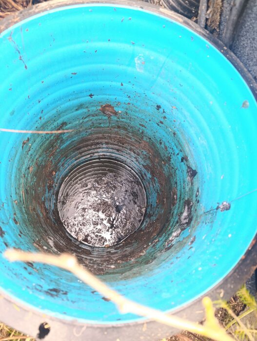 Öppen fördelningsbrunn med blå insida och lerig botten, placerad cirka 7-8 meter från trekammarbrunnen vid ett hus.