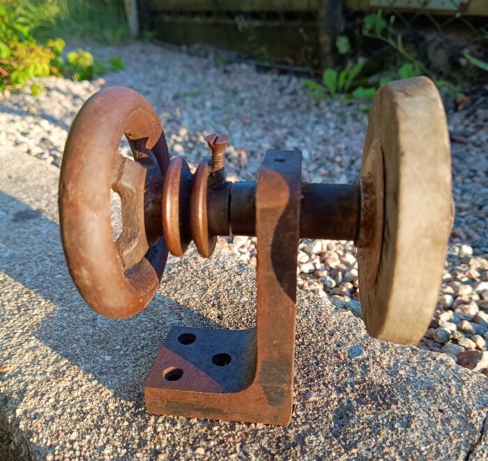 Liten rostig remdriven slipmaskin i gjutjärn, placerad utomhus på en cementyta.