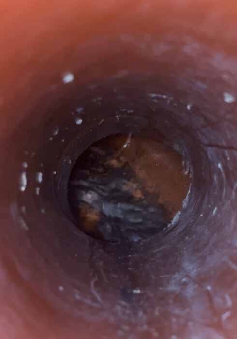 Insidan av ett dagvattenrör med lite stillastående vatten i botten, sett från övre kant av ett vertikalt uppstick.