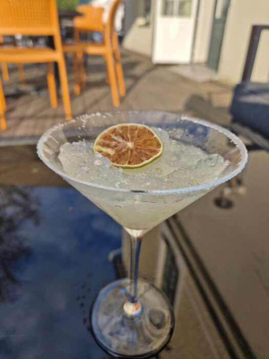 Frozen Margarita med torkad apelsinskiva som dekoration, serverad i cocktailglas utomhus på ett bord.
