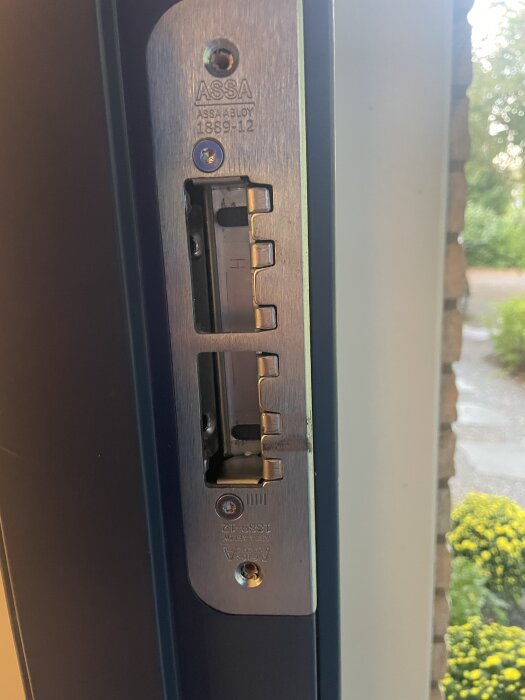 Dörrbleck av märket ASSA ABLOY fastskruvat i en dörrkarm. Skruvar synliga, installation av Nimly-lås pågår.
