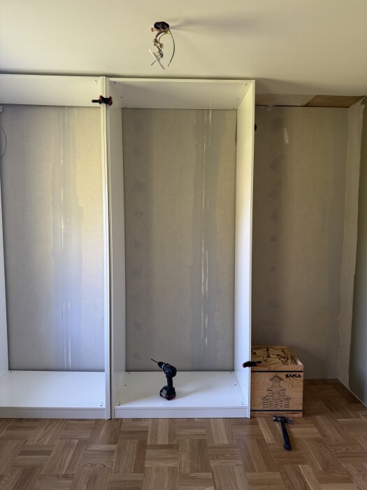 Montering av garderob med verktyg: borrmaskin, snabbtving och kaplastavar. På golvet bredvid ses en hammare och en låda med stavar.