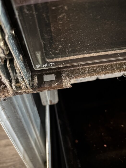 Utsidan av en ugnslucka från Cylinda där tre metallfästen ska monteras. Innerdelen av luckan sitter kvar, märket Schott syns på glaset.