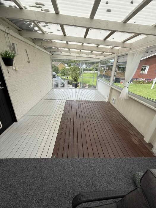 Målad altan med vit och brun yta, skjutpartier flyttade för en enhetlig, större känsla. Vit vägg, träbjälkar, fönster och utsikt över trädgård.