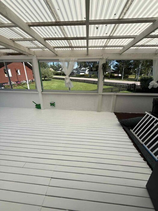 Nyomålat altangolv med vit färg, solbelyst och utan tidigare uppdelning mellan ute- och innedel. Gröna marker och ett rött hus i bakgrunden.