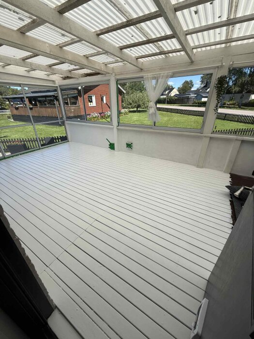 Nymålat golv på altan med enhetlig vit yta, skjutpartier har flyttats. Bakgrund med gräsmatta och hus synlig genom fönstren.