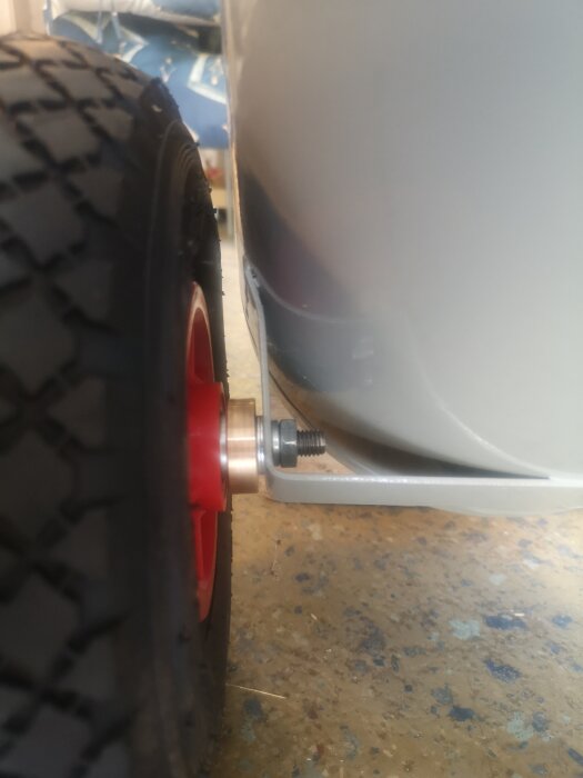 Hjulaxel på kompressor med svarvad bussning vid fästpunkten, vilket underlättar rörlighet över grus.