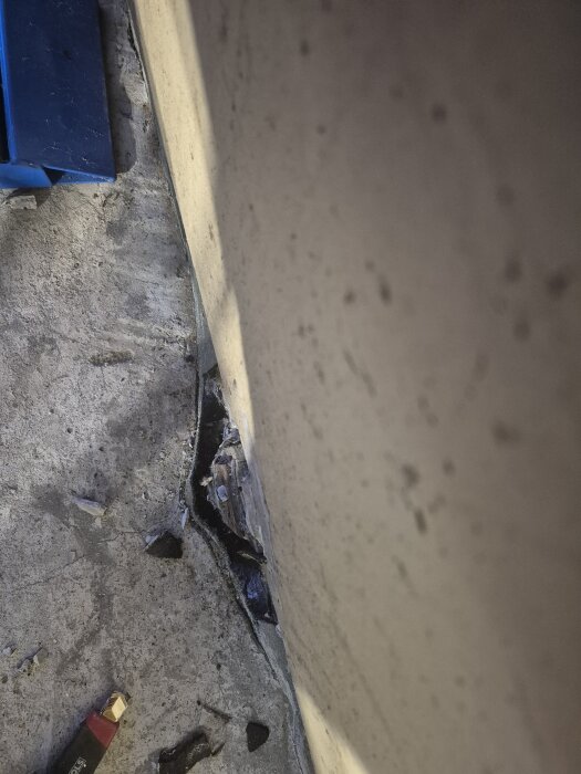 Glipa mellan betonggolv och garagevägg, delvis fylld med materialbitar. Verktyg synligt till vänster, osäker konstruktion diskuteras.