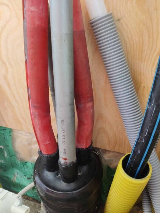 System av färgglada vattenrör och ledningar i ett träskåp, med rör skyddade av svarta muffar.