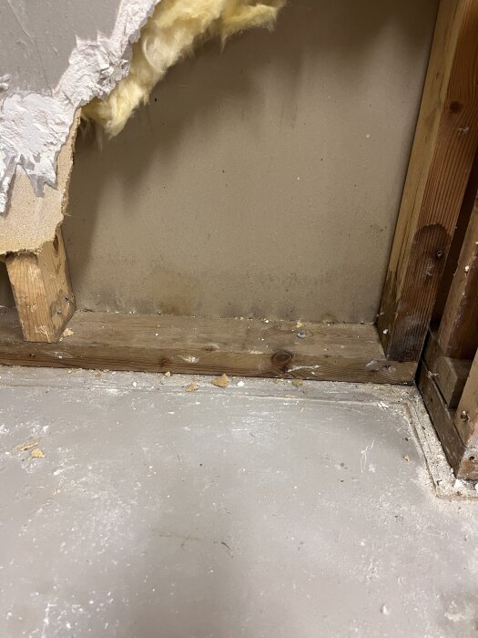 Riven gipsvÀgg vid garageport med trÀstomme synlig samt gul isolering; arbete pÄgÄr med att renovera garageutrymmet.