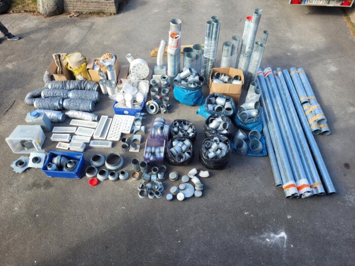 Olika ventilationsrör, delar och tillbehör uppställda på marken, inklusive spirorör, kanaler och kopplingar för ventilationsinstallationer.