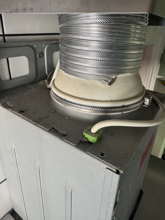 Köksfläkt med synligt ventilationsrör och sladd ovanpå, ansluten till ett fläktaggregat i kök.