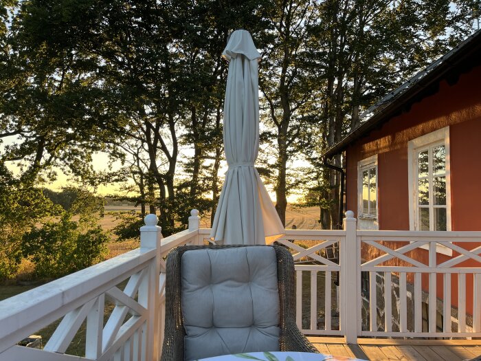 Solnedgång på en nyrenoverad balkong med en solstol och ett paraply i förgrunden, samt en röd byggnad till höger.