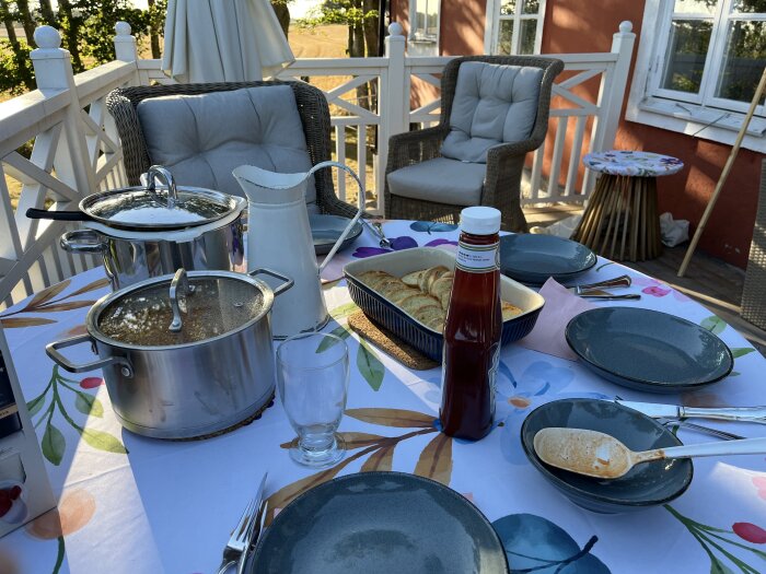 Bord på en balkong dukat för middag med kastrull med spaghetti och köttfärssås, tallrikar, ketchupflaska och tillbehör.