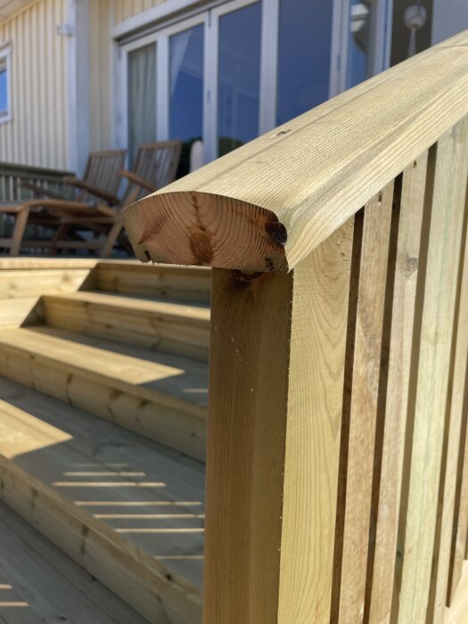 Träaltan med sluttande handledare utan gerad ände, omgivande räcke och altandörrar i bakgrunden, fotograferad i dagsljus.