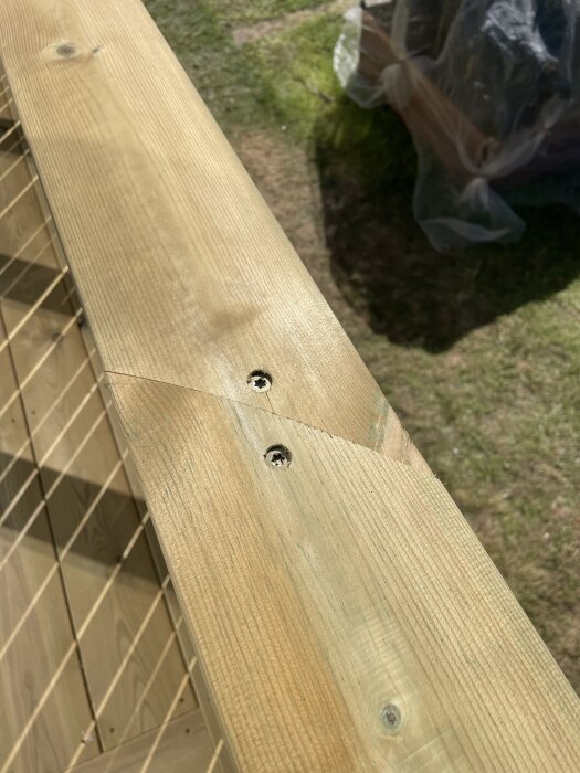 Altanräcke med ändträ och skruvhål, delvis avslutat med sågskärning, visar montering utan hörnlist, trädäck synligt i bakgrunden.