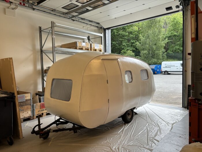 Vitmålad vagn inomhus med täckta fönster och en garageport öppen mot en parkering. Verkar vara en del av ett renoveringsprojekt.