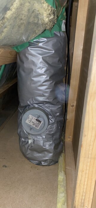 Isolerad avluftningskanal framför vägg, med grått skyddsmaterial och etikett, i samband med byte av frånluftsvärmepump.