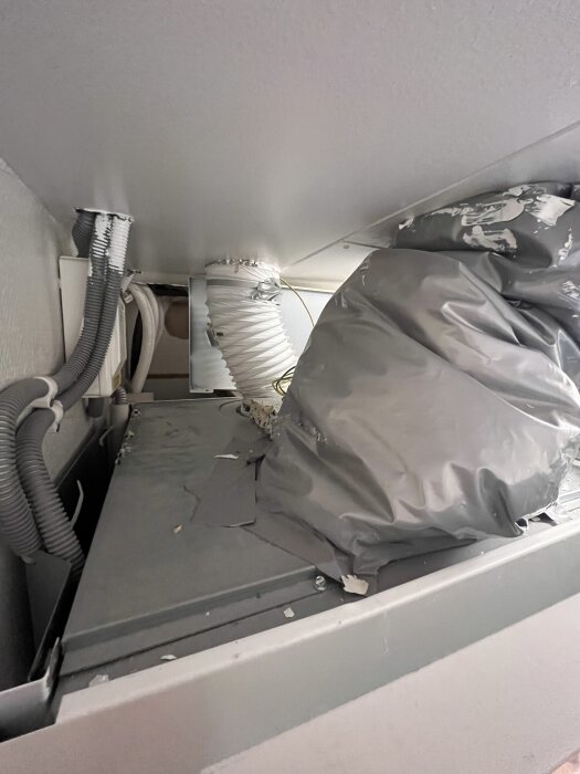 Avluftningskanal med isolering ansluten till frånluftsvärmepump, omgiven av diverse kablar och rör i ett begränsat utrymme.