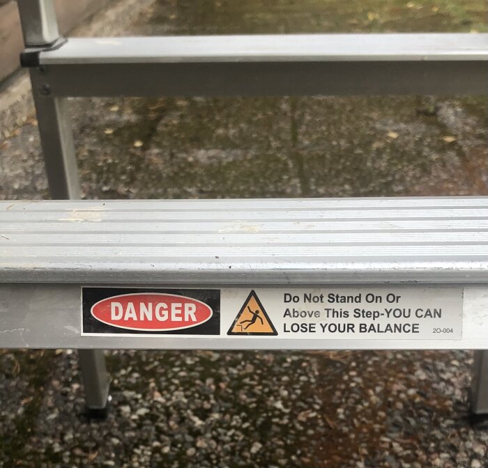 Aluminiumstege med varningsskylt: “FARA. Stå inte på eller ovanför detta steg, du kan tappa balansen.”