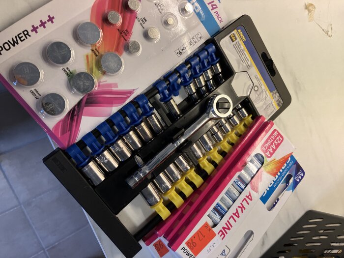 Spärrhandtag och hylsor med blå märkning, knappcellsbatterier och AAA-batteripack på ett bord.