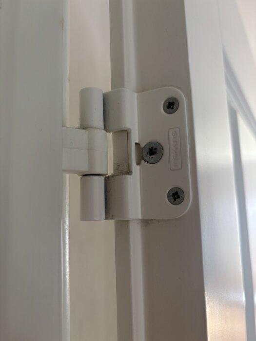 Vit dörrgångjärn med två synliga skruvar, fråga om att ta bort dörren utan att skruva ur skruvarna.