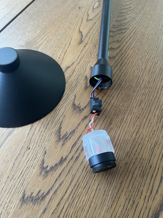 Svart lampa med exponerade kablar på ett träbord, nära en kretskomponent.