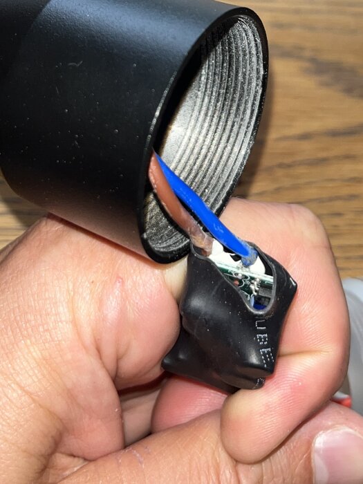 Närbild på handen som håller en svart armaturdel, med blå och brun kabel synliga inuti.