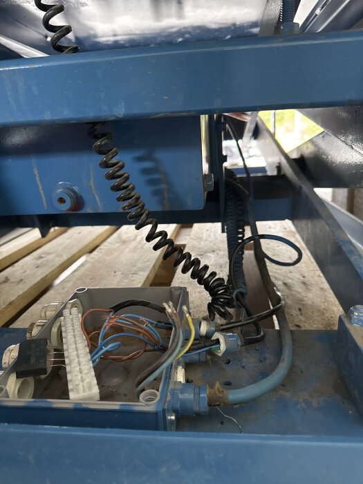 Blå maskindel med exponerad elektronik och kablar i en kopplingsdosa.