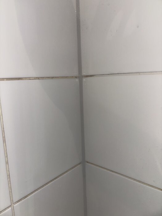 Fog i duschhörn med missfärgningar och skador på foglinjerna på vita kakelplattor i ett badrum.
