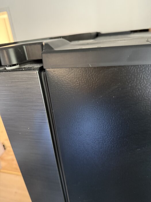 Närbild av en side by side kylskåpsdörr med svart och metallisk yta, del av ett projekt att bygga in kylskåpet i väggen.