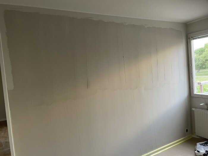 Ospacklad vägg med ojämn målning under fönster, nära tak och golv; oro över att arbetet inte avslutats korrekt.
