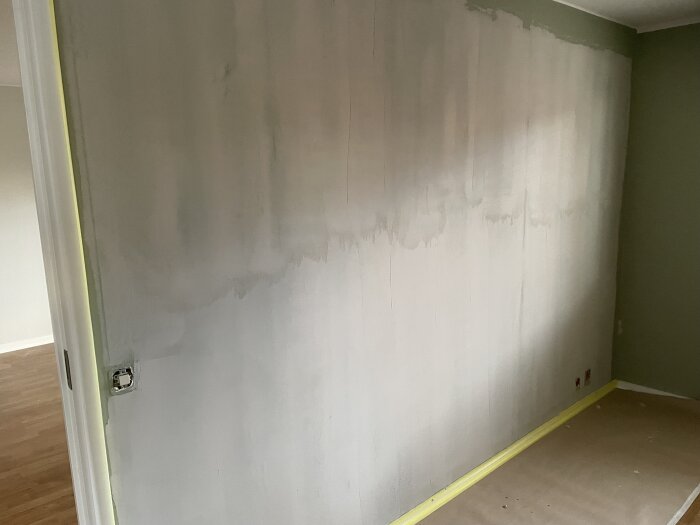 Vägg med ofullständigt spackelarbete, ej färdigmålad hela vägen upp till taket. Täckpapp och tejp finns vid golvet.