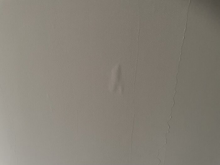 En vägg med ojämn struktur där spackel inte når ända upp till taket, med en synlig ojämnhet eller buckla i mitten.