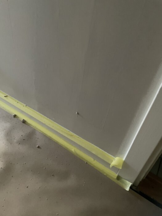 En halvspacklad vägg med bristfälligt arbete nära taket och gul målartejp vid golvet.