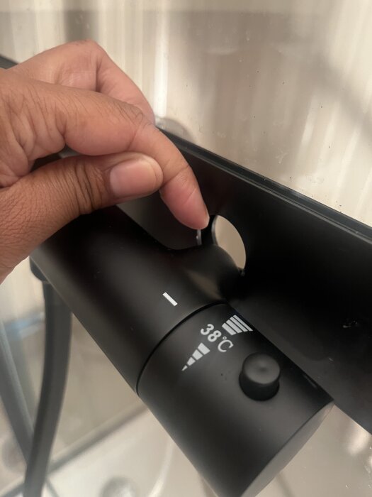 Hand pekar på område vid en termostatblandare där vatten läcker, med temperaturinställning synlig.