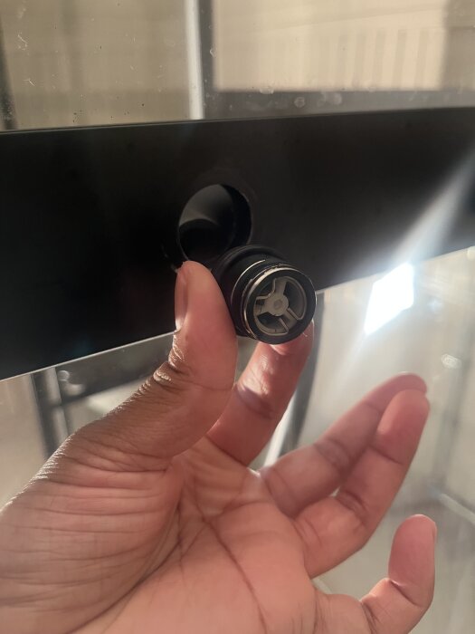 Hand som håller en silvrig koppling vid ett hål, vilket är platsen där det läcker vatten enligt beskrivningen.