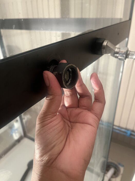 Hand som håller en svart hylsa vid koppling på glasytan, fokus på området för vattenläckage.