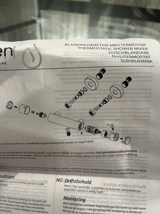 Instruktionsblad för duschblandare med termostat, visar sprängskiss av komponenter och text om installation och driftsförhållanden på flera språk.