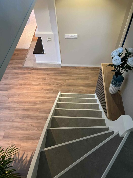Nyrenoverad trappa med mörkt golv, träväggpanel och en vacker vas med vita rosor placerad på ett bord vid sidan.