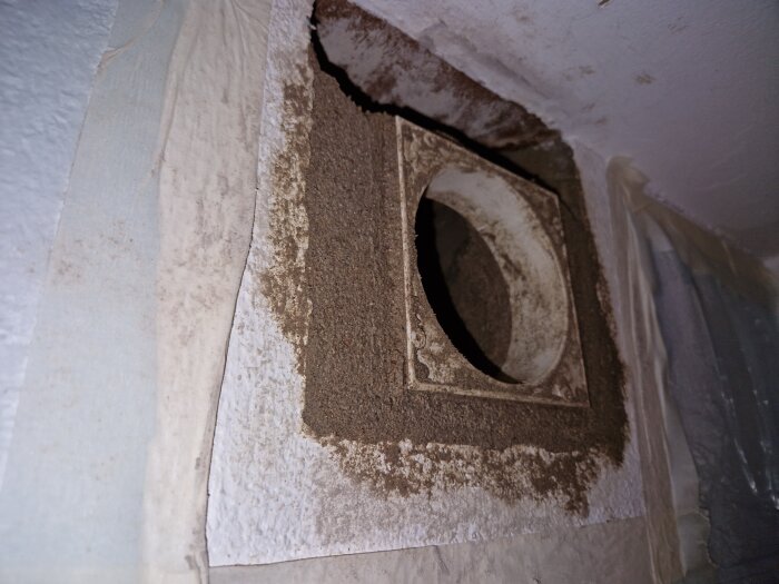 Ett hål i en vägg för en ventil, med synligt gips och bruk runt om, i ett byggprojekt för installation av en inre del i ventilationssystemet.