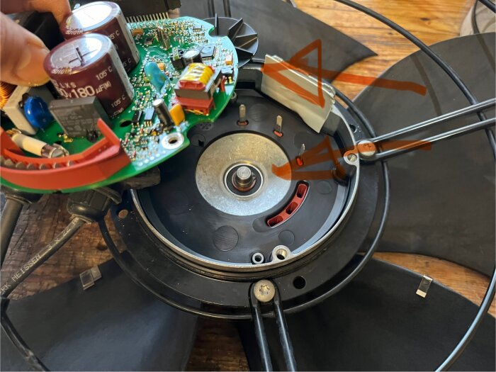 Elektronikkrets ovanpå fläkt med svart plast avdragen, låsring synlig. Röda pilar pekar på komponenter.